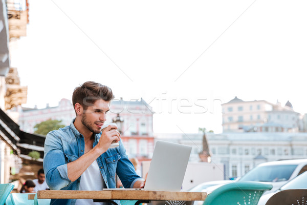Smiling cheerful casual man using laptop outdoors and drinking coffee Stock photo © deandrobot