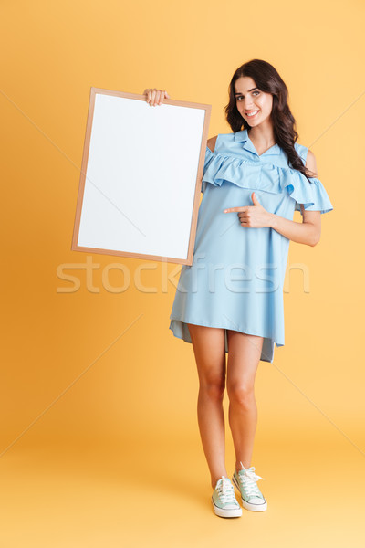 Cheerful woman in blue dress pointing finger at white board Stock photo © deandrobot