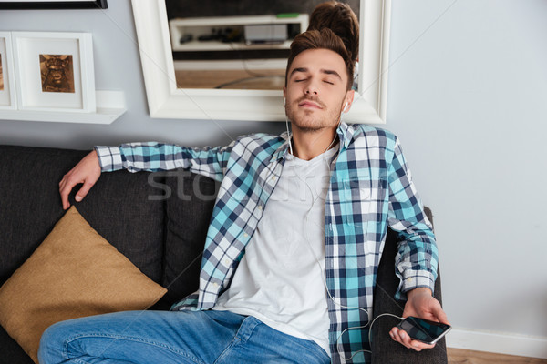 Relaxed man listening music with earphones and using smartphone Stock photo © deandrobot
