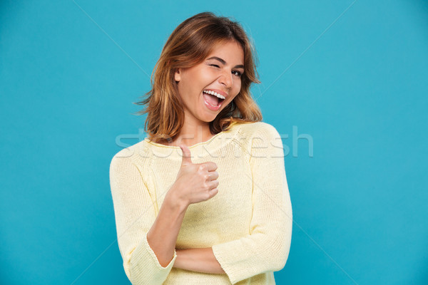 Cheerful woman in sweater showing thumb up and winks Stock photo © deandrobot