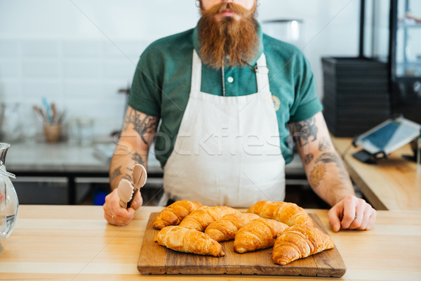 Bearded man in apron standing and holding tongs for croissants Stock photo © deandrobot