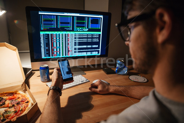 Serious developer in glasses using computer and smartphone  Stock photo © deandrobot