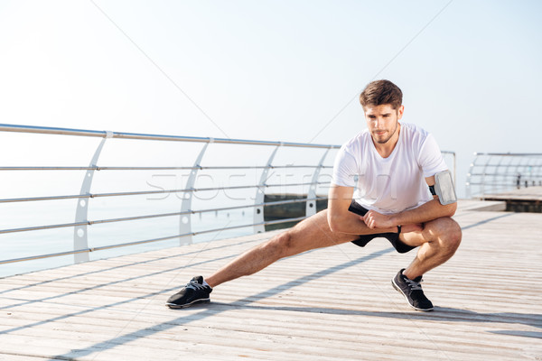 Young sportsman stretching legs during workout on pier Stock photo © deandrobot