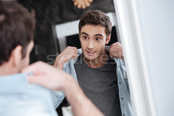 Man looking at himself in mirror and holding his collar Stock photo © deandrobot
