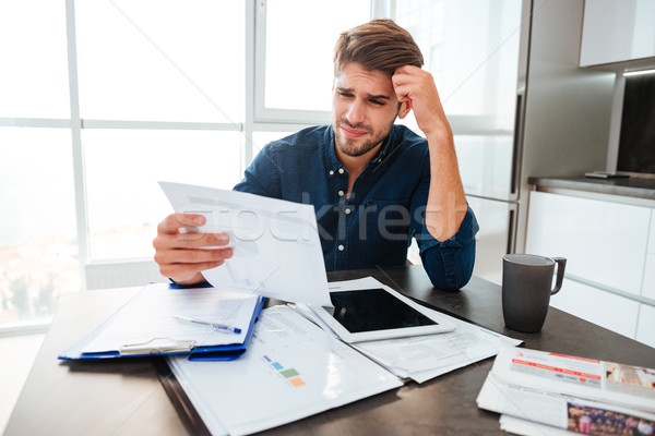 Confused man holding head with hand and looking at documents Stock photo © deandrobot