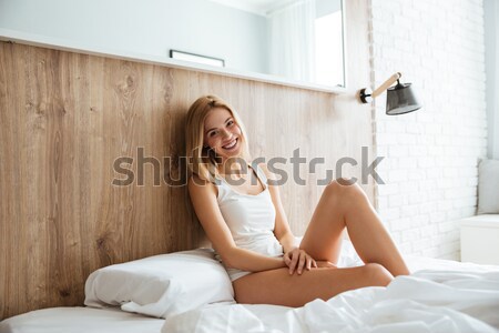 Happy relaxed young woman sitting on bed Stock photo © deandrobot