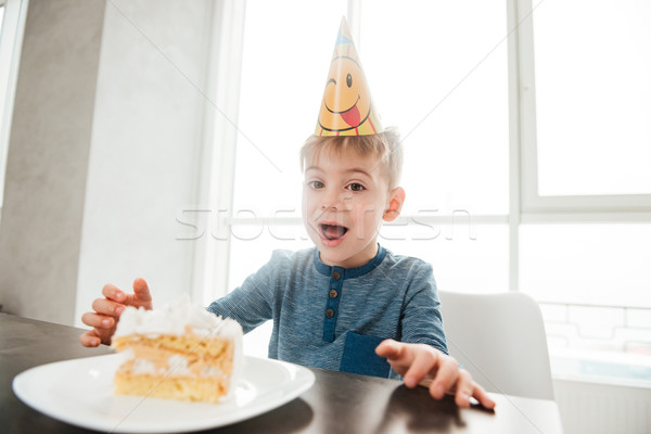 Happy birthday boy sitting in kitchen near cake and eating. Stock photo © deandrobot