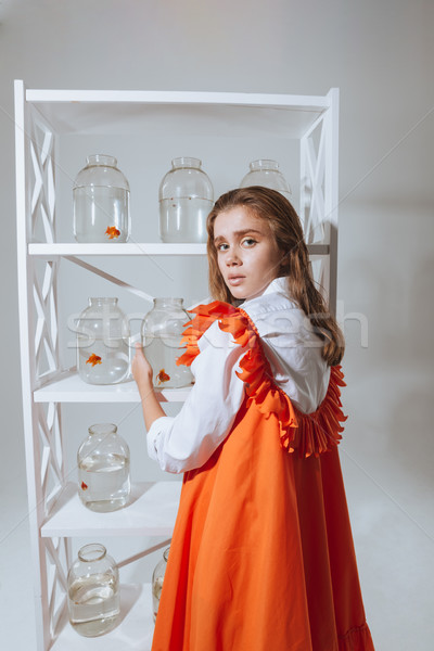 Beautiful young woman taking jar with gold fish from closet Stock photo © deandrobot