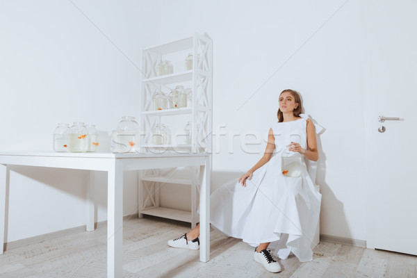 Stock photo: Pretty young woman sitting and holding gold fish in jar