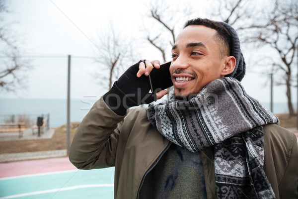 Young african man wearing hat talking by phone. Stock photo © deandrobot