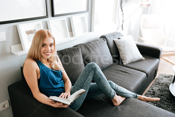 Femeie zambitoare relaxare lectură carte canapea acasă Imagine de stoc © deandrobot