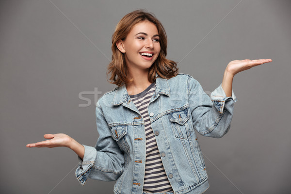 Young cheerful woman in jeans jacket looking at her empty palm Stock photo © deandrobot