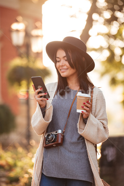 Cheerful asian girl in black hat and woolen cardigan checking ne Stock photo © deandrobot