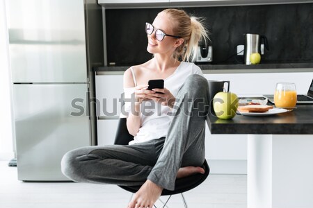 Full-length shot of young focused lady using smartphone while sitting in kitchen Stock photo © deandrobot