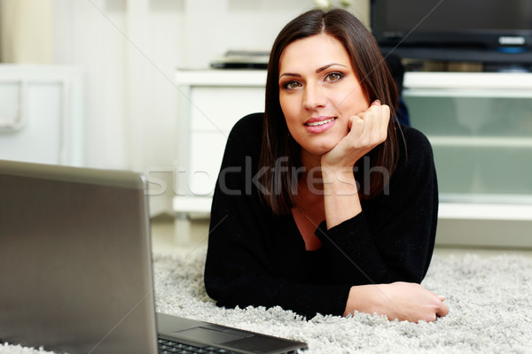 Middle-aged thoughtful woman lying on the carpet with laptop at home Stock photo © deandrobot