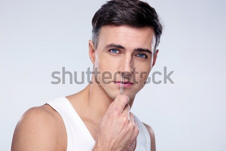 Stock photo: Man pucking nose hair with tweezers over gray background