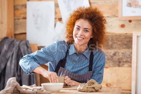 Stock photo: Cheerful woman potter sitting and working in art pottery studio