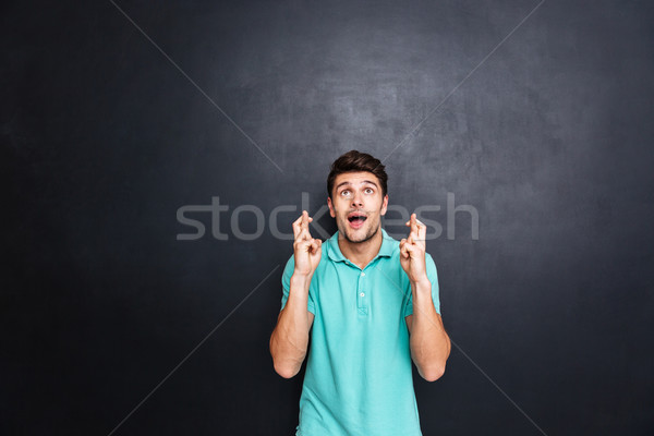Handsome young man with his fingers crossed isolated over black Stock photo © deandrobot