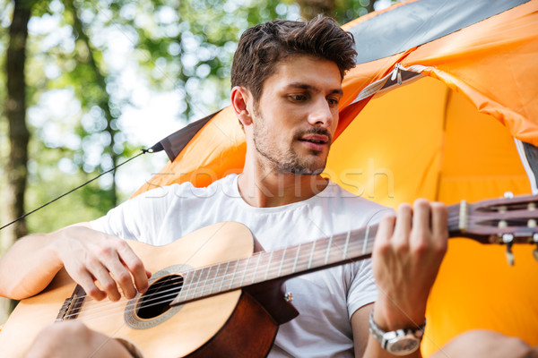 Handsome man tourist singing and playing guitar at touristic tent Stock photo © deandrobot