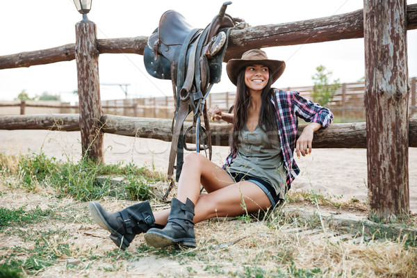 Stock photo: Smiling happy cowgirl sitting and resting at the ranch fence