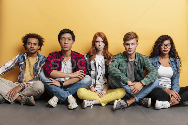 Groupe sérieux jeunes séance jambes croisées [[stock_photo]] © deandrobot