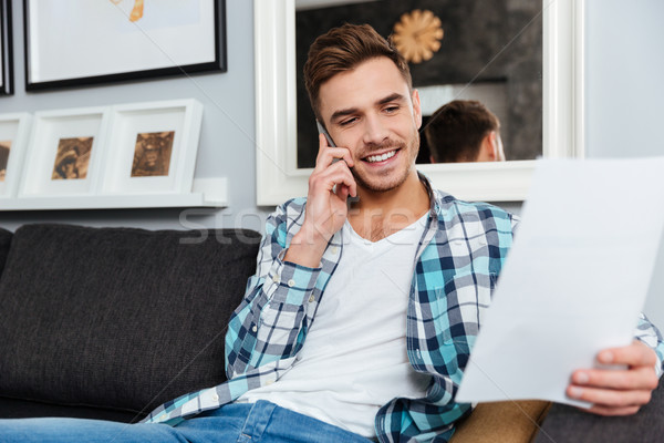 Handsome bristle man talking by phone while looking at documents. Stock photo © deandrobot