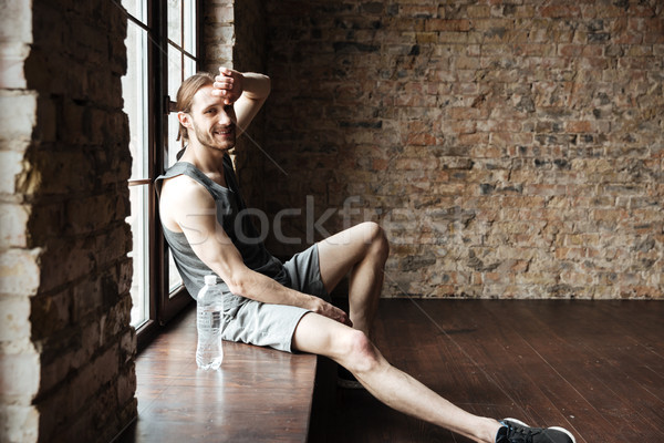 Smiling fitness man resting at the windowsill with water bottle Stock photo © deandrobot
