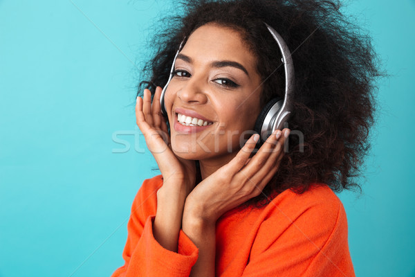 African american smiling woman in orange shirt listening to musi Stock photo © deandrobot