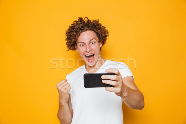 Joyful man 20s with brown hair screaming and clenching fist whil Stock photo © deandrobot