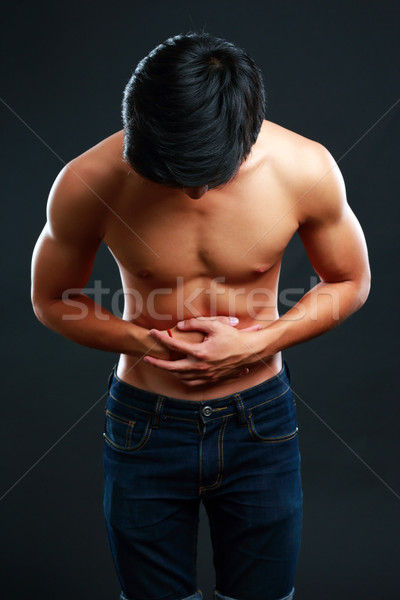 Young man holding his sick stomach in pain on black background Stock photo © deandrobot