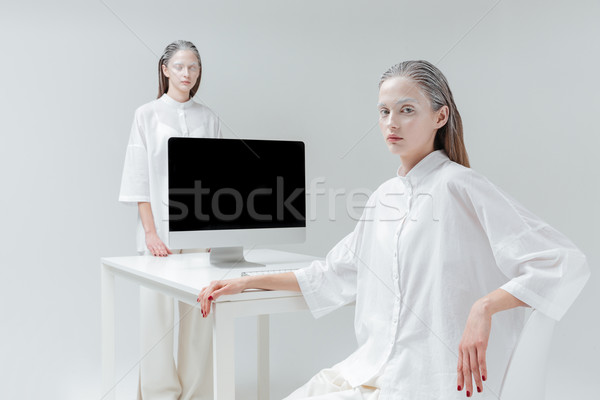 Two girls sitting and standing near the desk with computer Stock photo © deandrobot