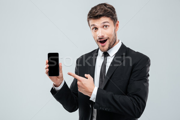 Amazed young businessman holding and pointing on blank screen smartphone Stock photo © deandrobot
