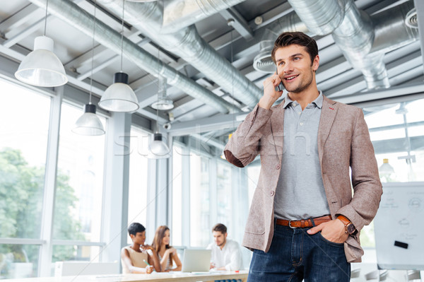 Happy young businessman talking on cell phone in office Stock photo © deandrobot