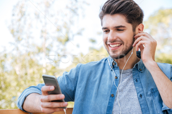 Young man sitting on the bench in park with phone Stock photo © deandrobot