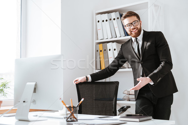 Attractive businessman holding chair. Look at camera. Stock photo © deandrobot