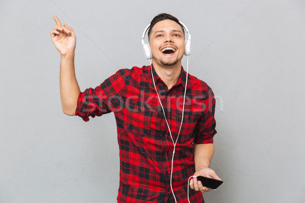Cheerful young man listening music with headphones. Stock photo © deandrobot