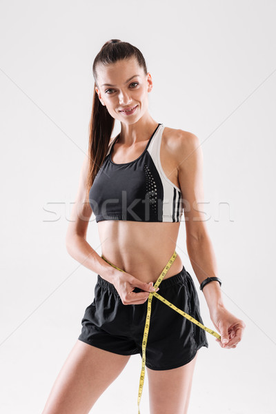 Portrait of a happy sportswoman measuring her waist Stock photo © deandrobot