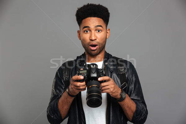 Amazed handsome afro american man in leather jacket holding digi Stock photo © deandrobot