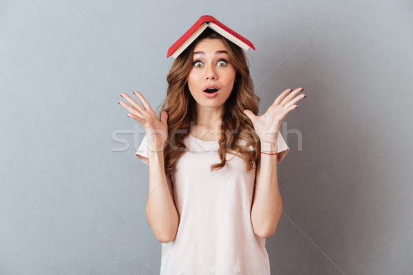 Portrait Of A Surprised Girl Holding Book On Her Head Stock