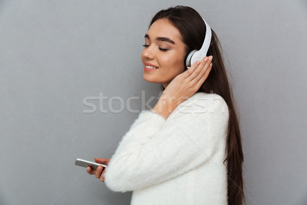 Side view of pleased brunette woman in sweater and headphones Stock photo © deandrobot