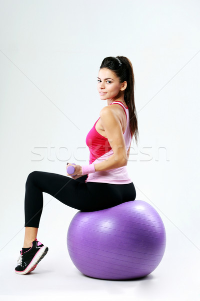 Side view of a young sport woman sitting on fitball with dumbells on gray background Stock photo © deandrobot