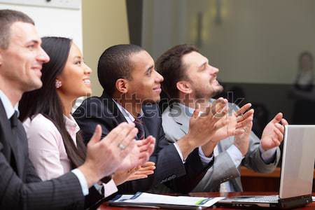 Multi ethnic business group greets you with clapping and smiling. Focus on woman Stock photo © deandrobot