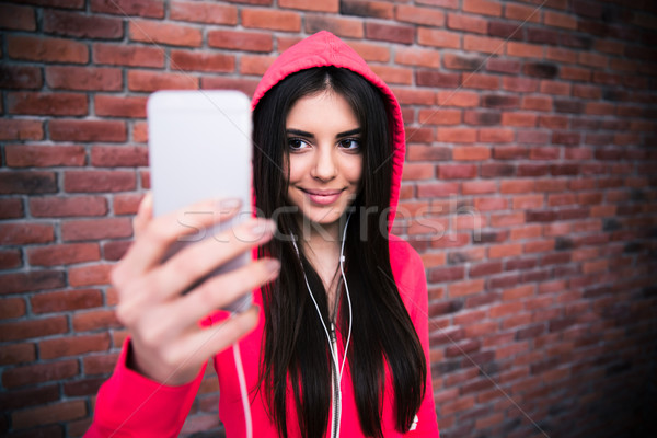 [[stock_photo]]: Femme · souriante · photo · mur · de · briques · regarder · smartphone