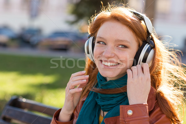 Happy smiling lady enjoying music on bench in park Stock photo © deandrobot