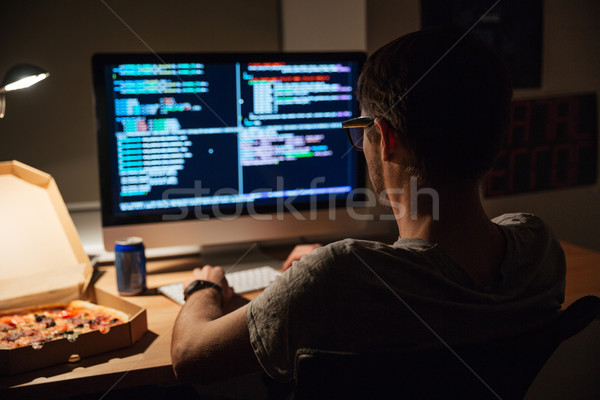 Back view of focused programmer writing code and eating pizza Stock photo © deandrobot