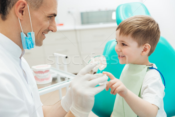 Cheerful man dentist demonstrating tooth brushing to little boy Stock photo © deandrobot