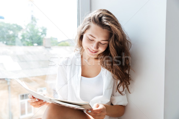 Charming young woman reading newspaper while siting on the windowsill Stock photo © deandrobot