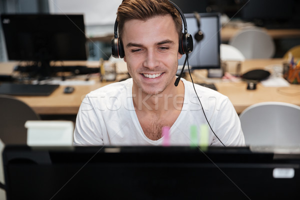 Hombre sesión ordenador auriculares sonriendo oficina Foto stock © deandrobot