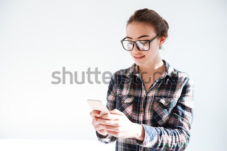 Smiling young woman in glasses standing and using mobile phone Stock photo © deandrobot