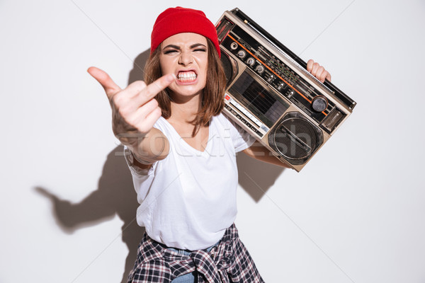 Young angry woman holding tape recorder and showing middle finger Stock photo © deandrobot